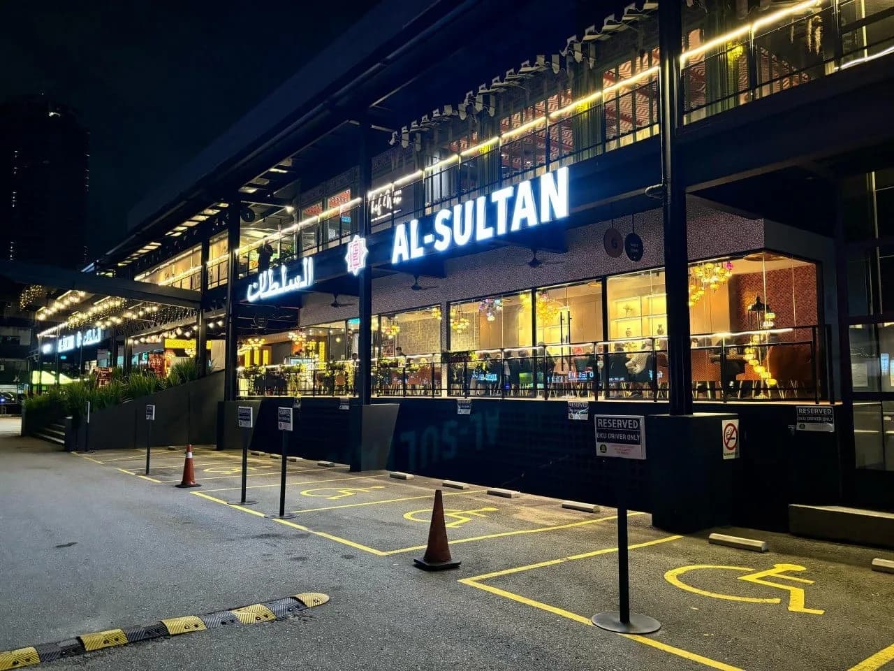 Al-Sultan Restaurant storefront at night with lit signage and dining area visible through windows