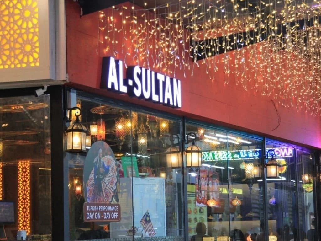 Al-Sultan Restaurant storefront at night with red facade, glowing white signage, and hanging golden lights