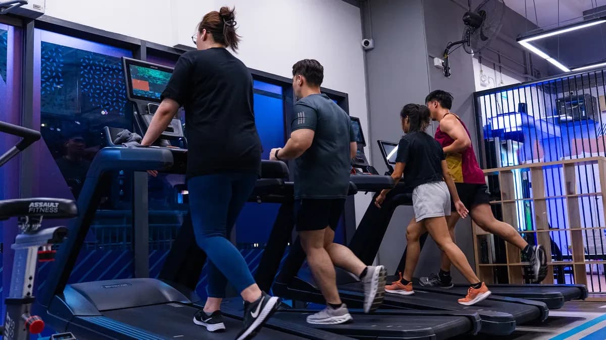 Gym members running on treadmills in a modern fitness facility with blue lighting