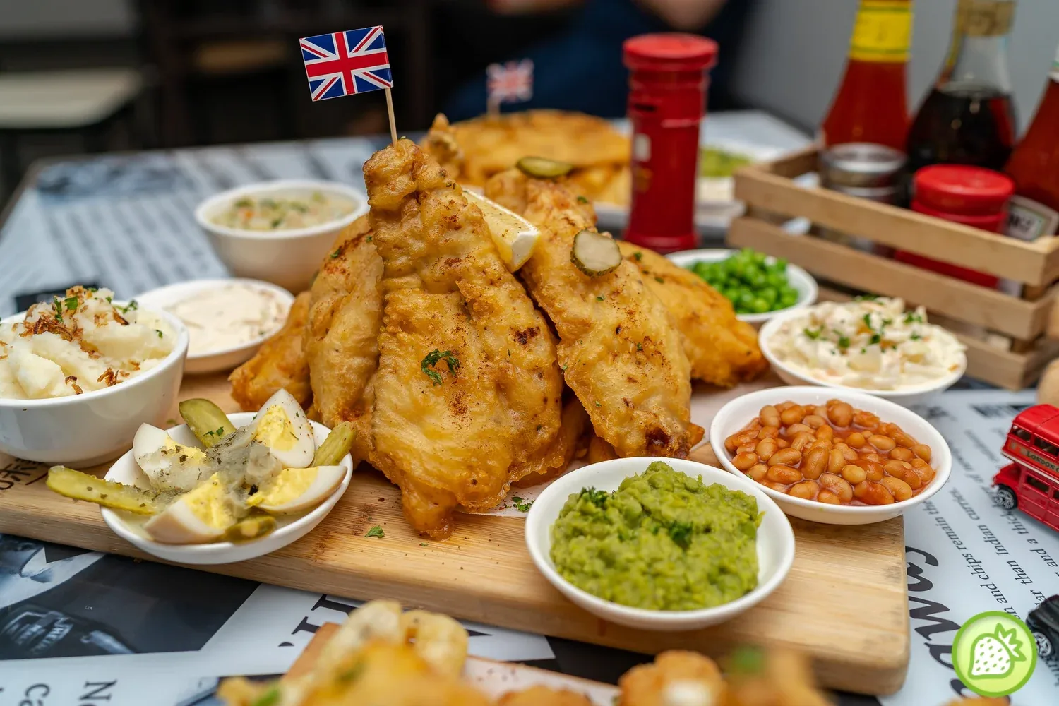 Golden fried fish with Union Jack flag, served with mushy peas, beans, and potato sides on wooden board