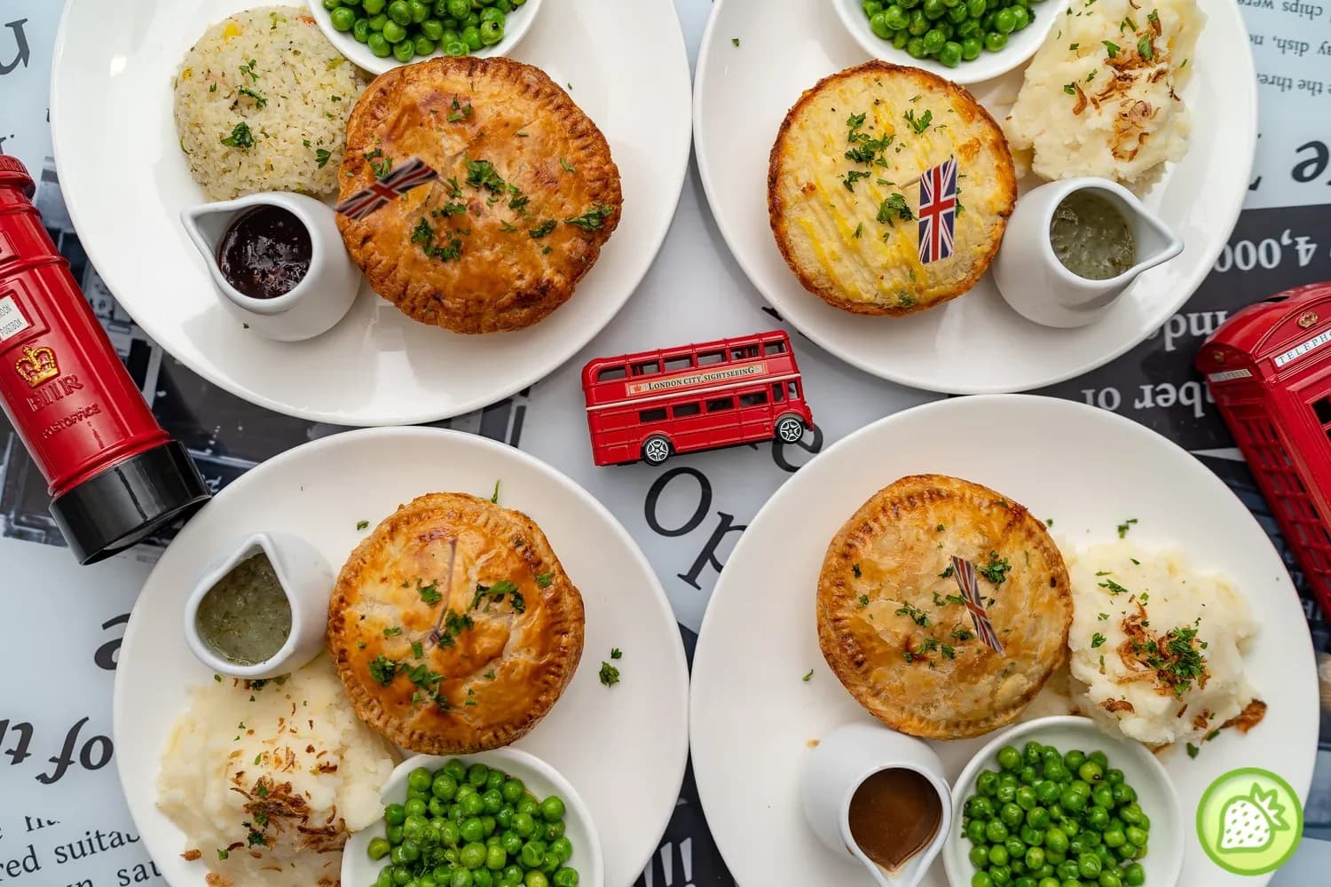 Four plates of British meat pies with sides and gravy on white plates