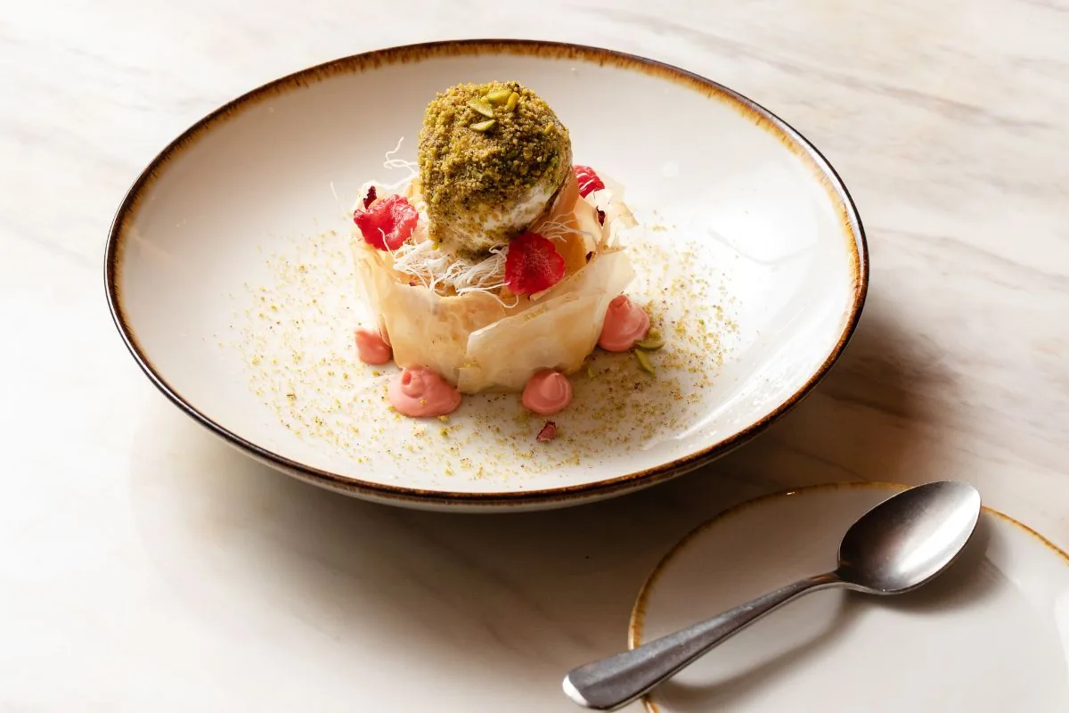 Fine dining dessert with pistachio dome, cream base, and red fruit garnish on white plate