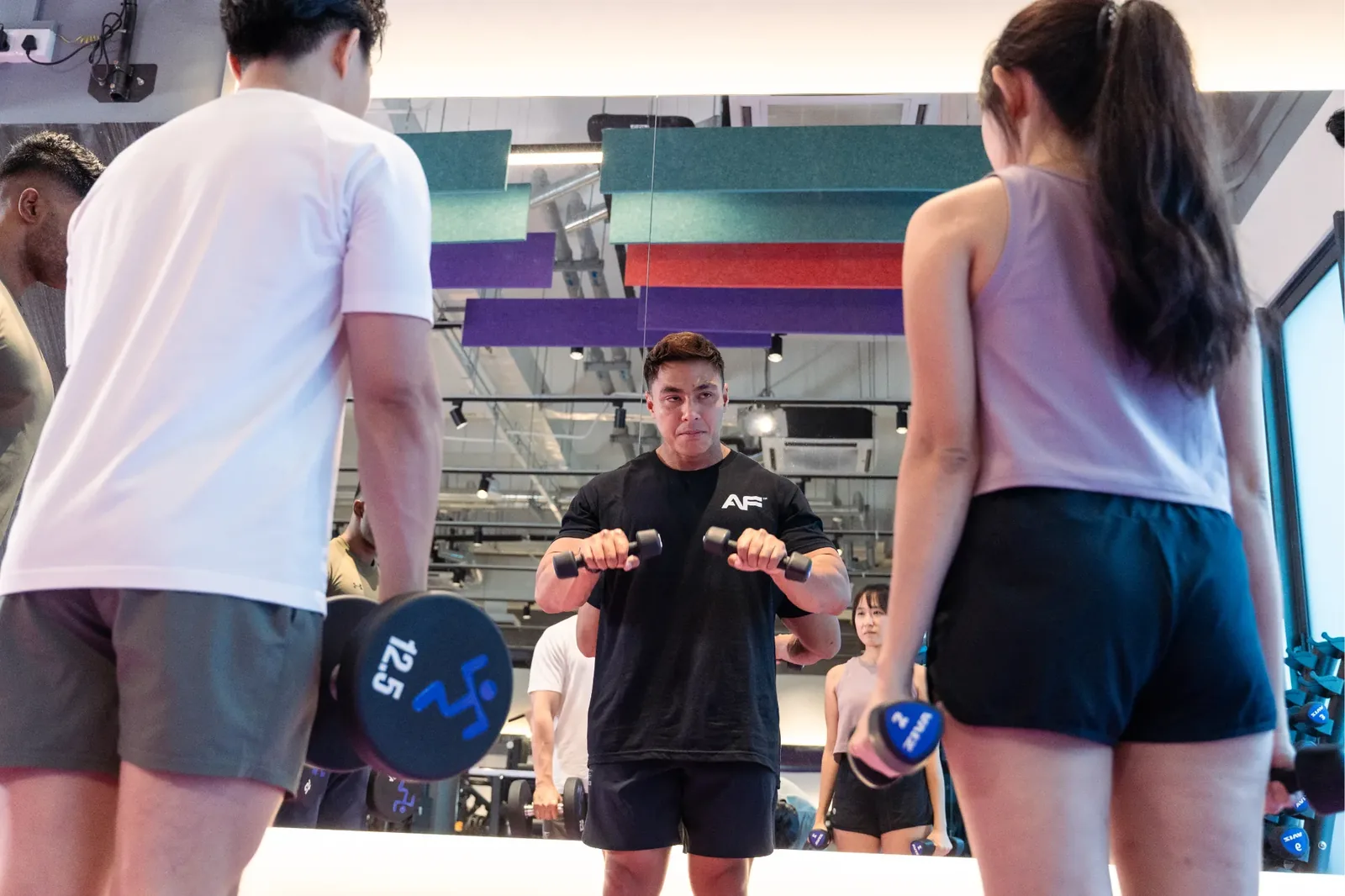 Fitness instructor directing group dumbbell class in bright gym studio