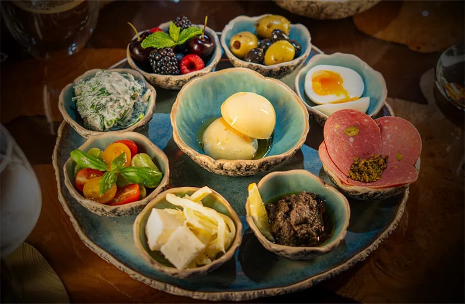 Charcuterie platter with cured meats, cheeses, olives, berries, and mezze in ceramic bowls