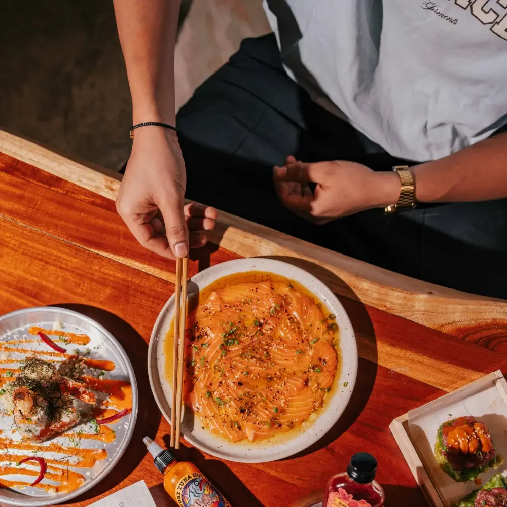 Diner with chopsticks eating noodle dish at wooden table with multiple Asian appetizers