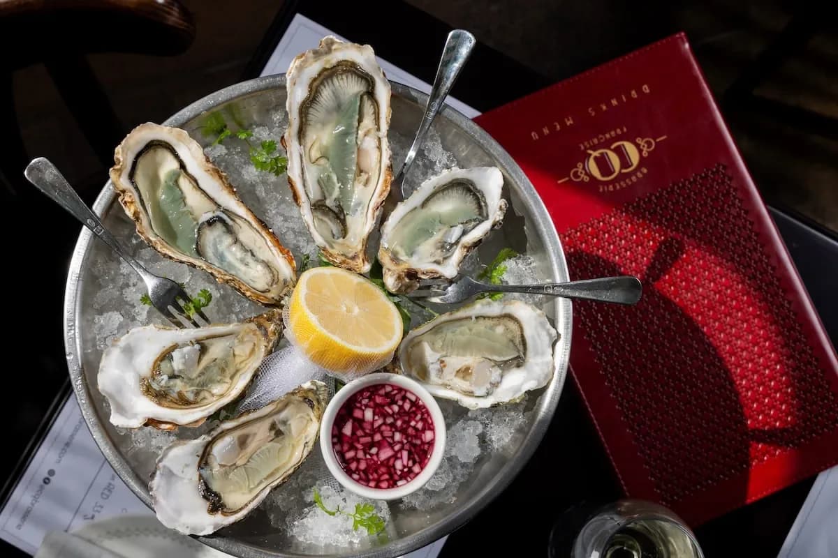 Oyster platter on ice with lemon, pomegranate seeds, and restaurant menu