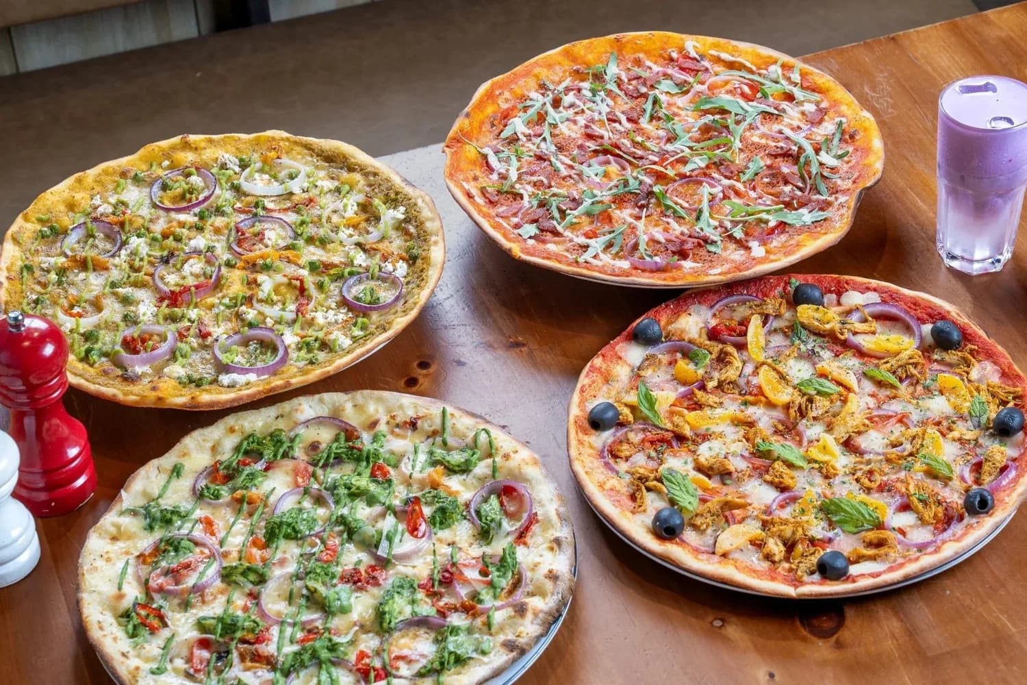 Four pizzas with different toppings arranged on a wooden table in a restaurant setting