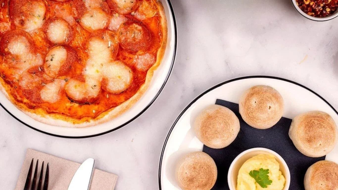 Pepperoni pizza and bread rolls with dipping sauce on white plates