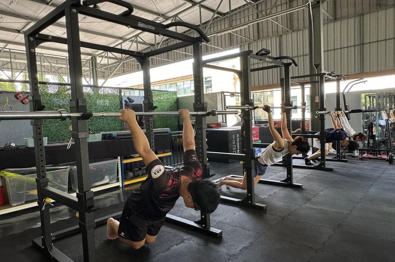 People doing pull-ups and exercises at outdoor gym stations with metal frames
