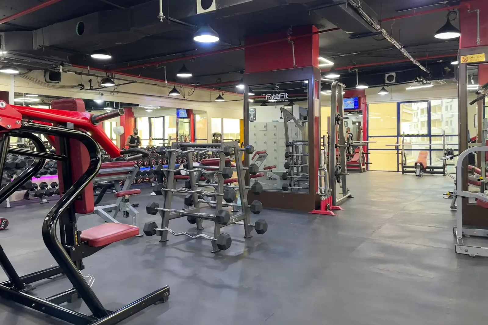 Spacious gym interior with red weight machines, dumbbells, and cardio equipment under bright industrial lights