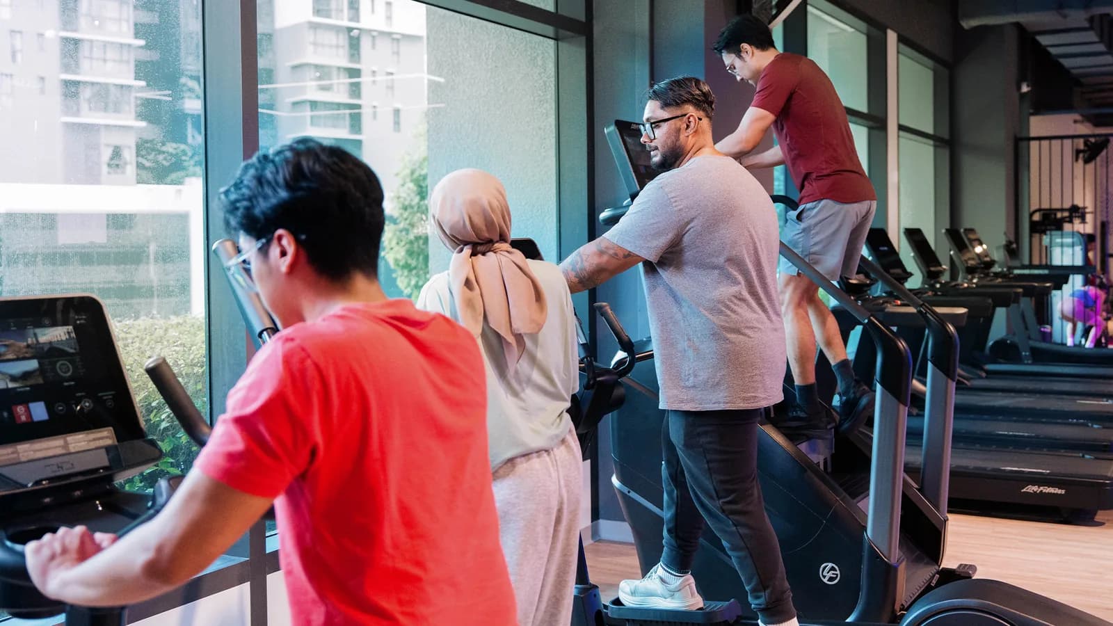 Fitness trainer helping a member use cardio equipment in a bright gym with city views