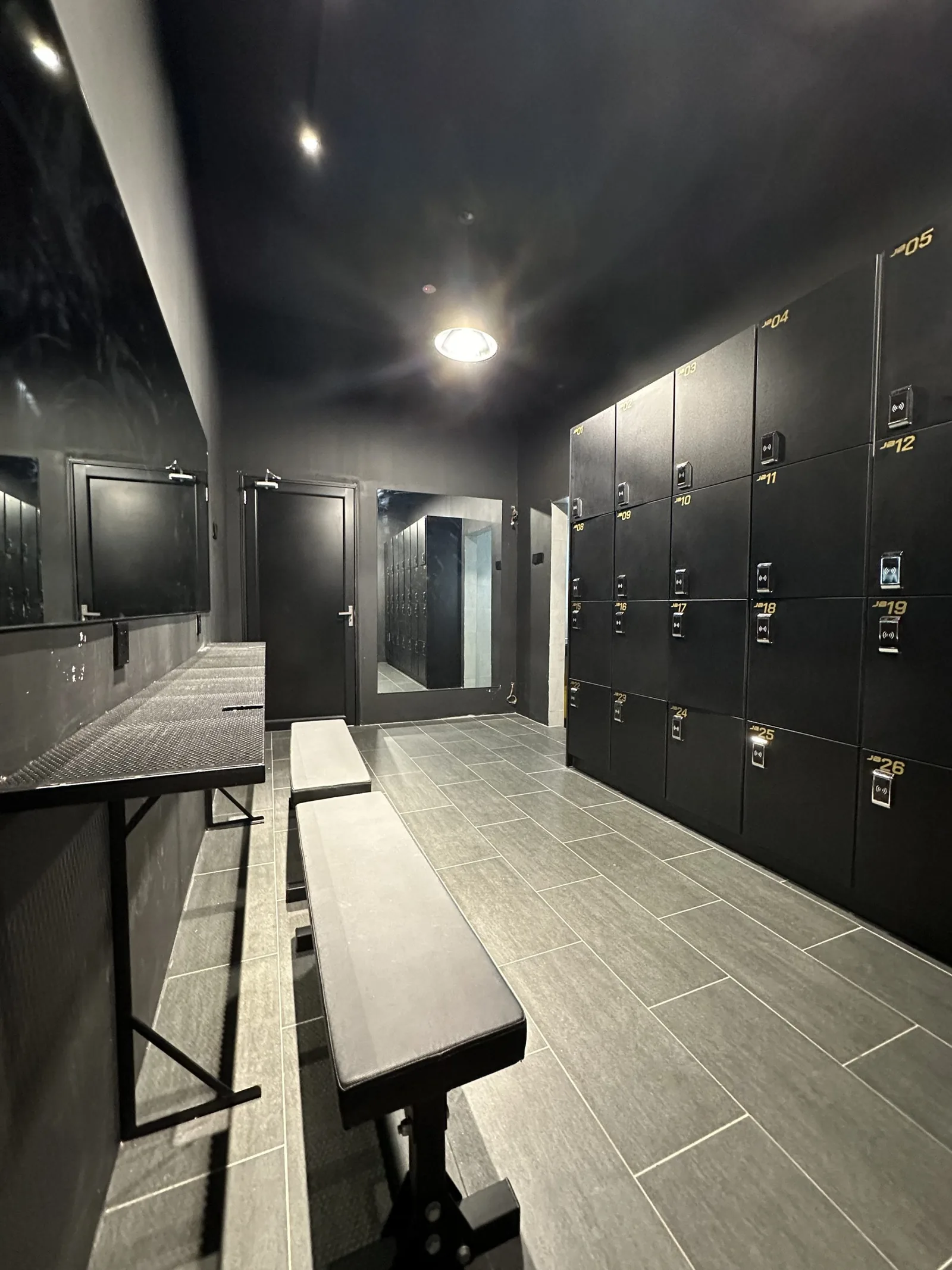 Modern gym locker room with black numbered lockers, benches, and tiled flooring