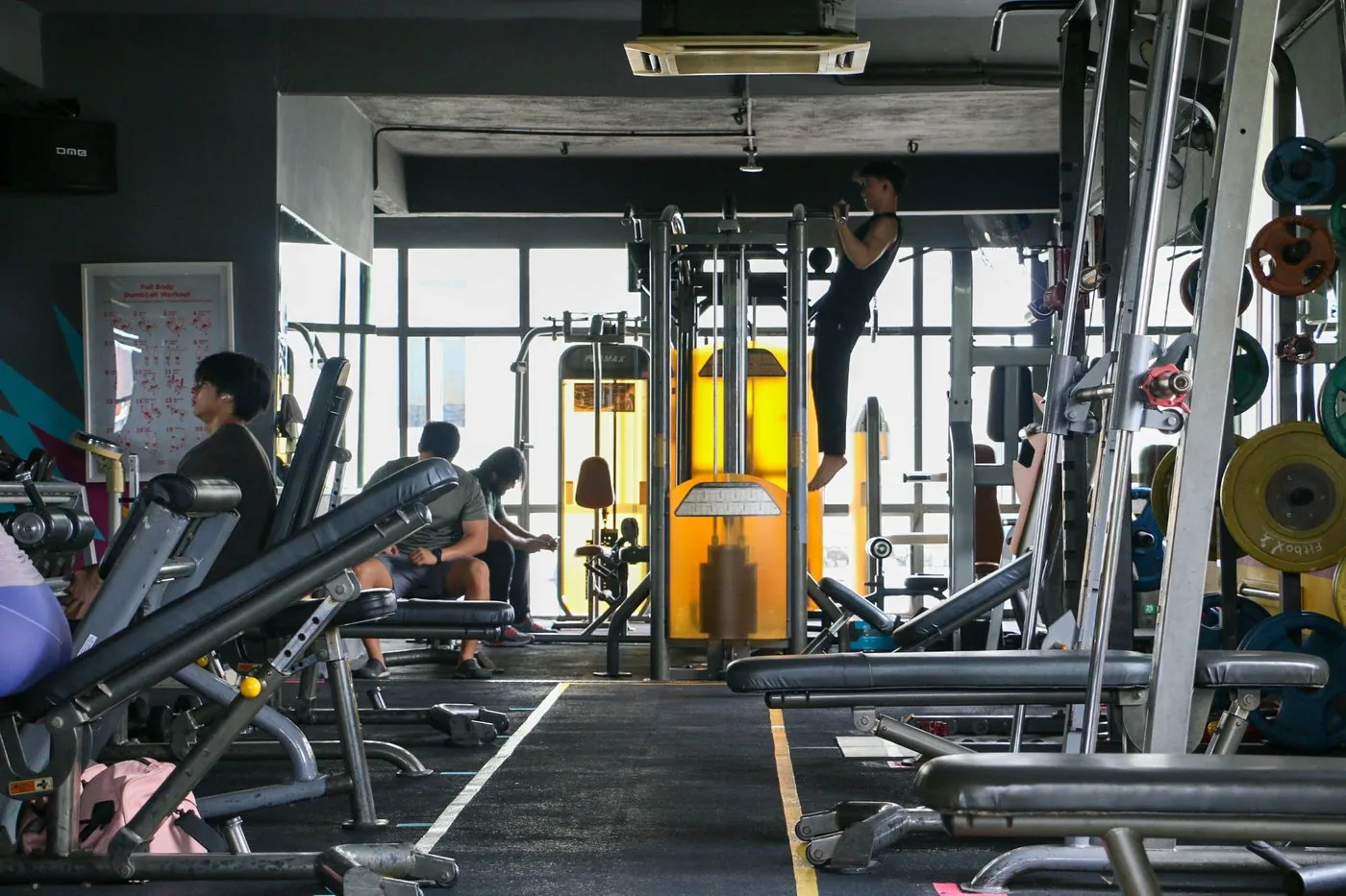 Gym members exercising on machines and equipment in a bright, modern fitness facility.