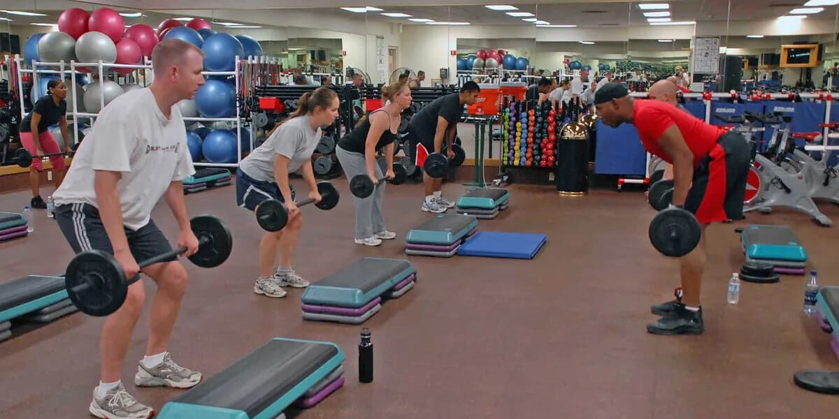 Group fitness class with participants doing dumbbell exercises on step platforms in a modern gym studio