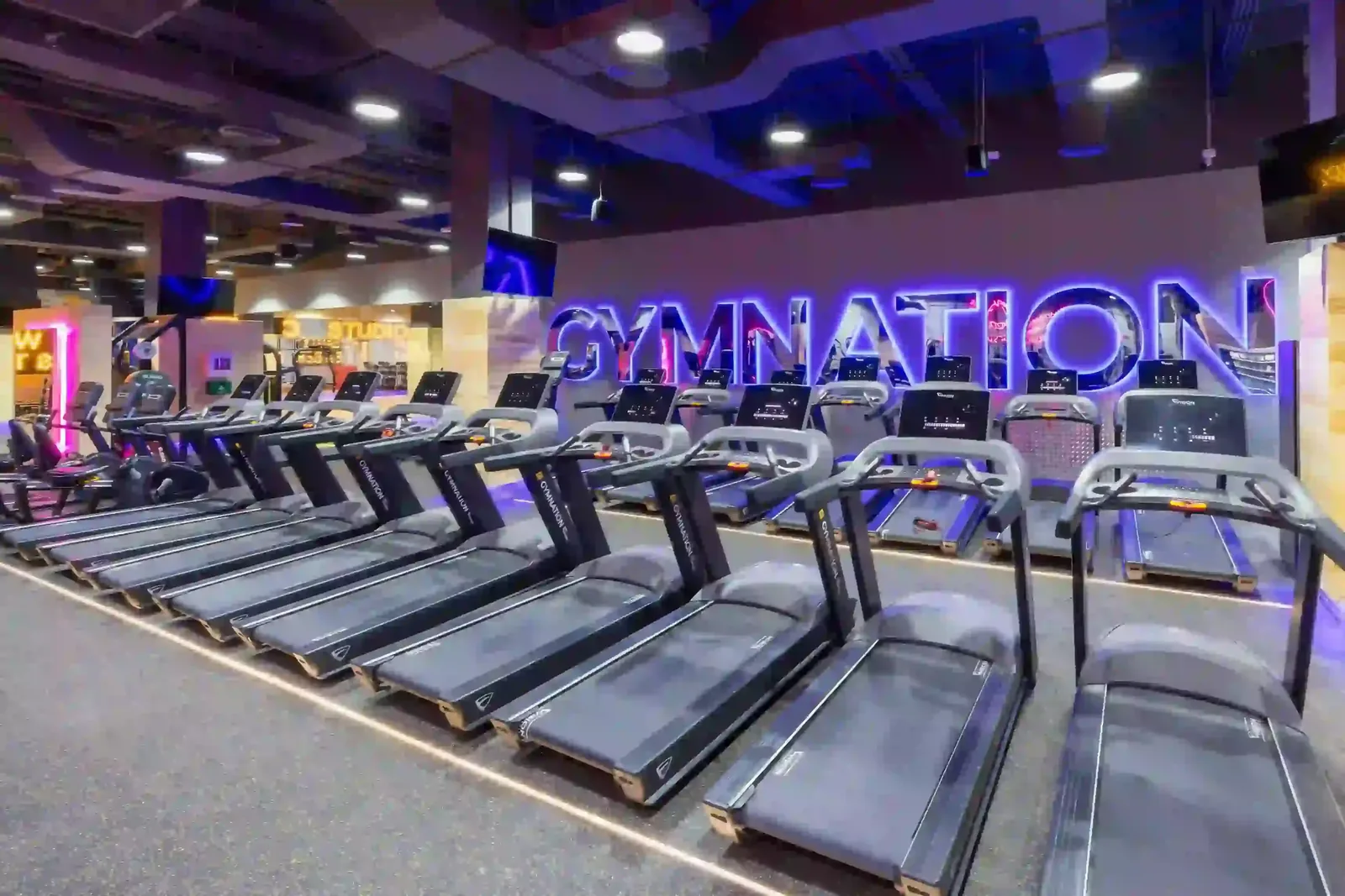 Treadmill area in modern gym with purple neon signage and blue lighting