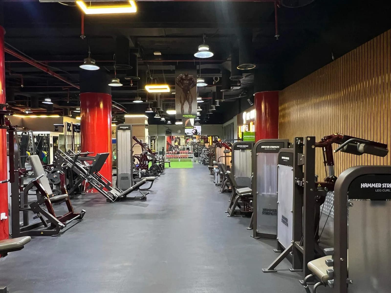 Spacious gym interior with rows of exercise machines, red pillars, and modern lighting