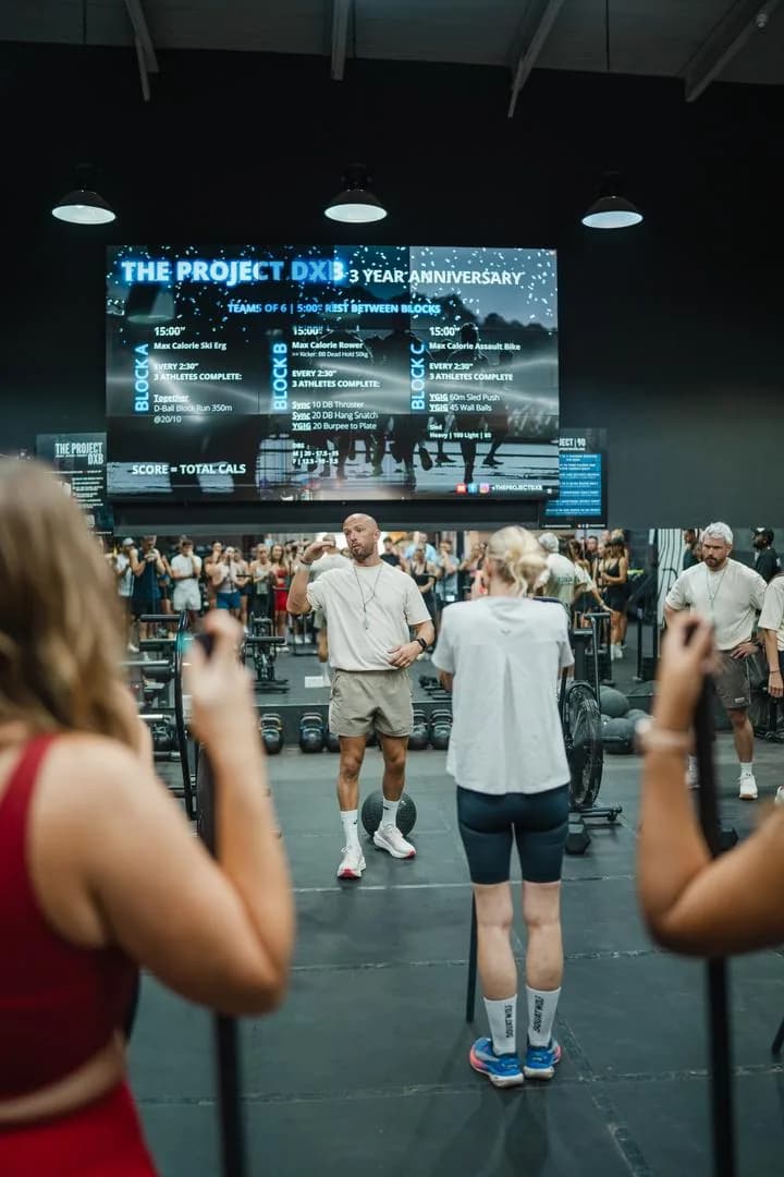 Instructor and participants doing fitness exercises in bright gym studio with scoreboard showing workout data