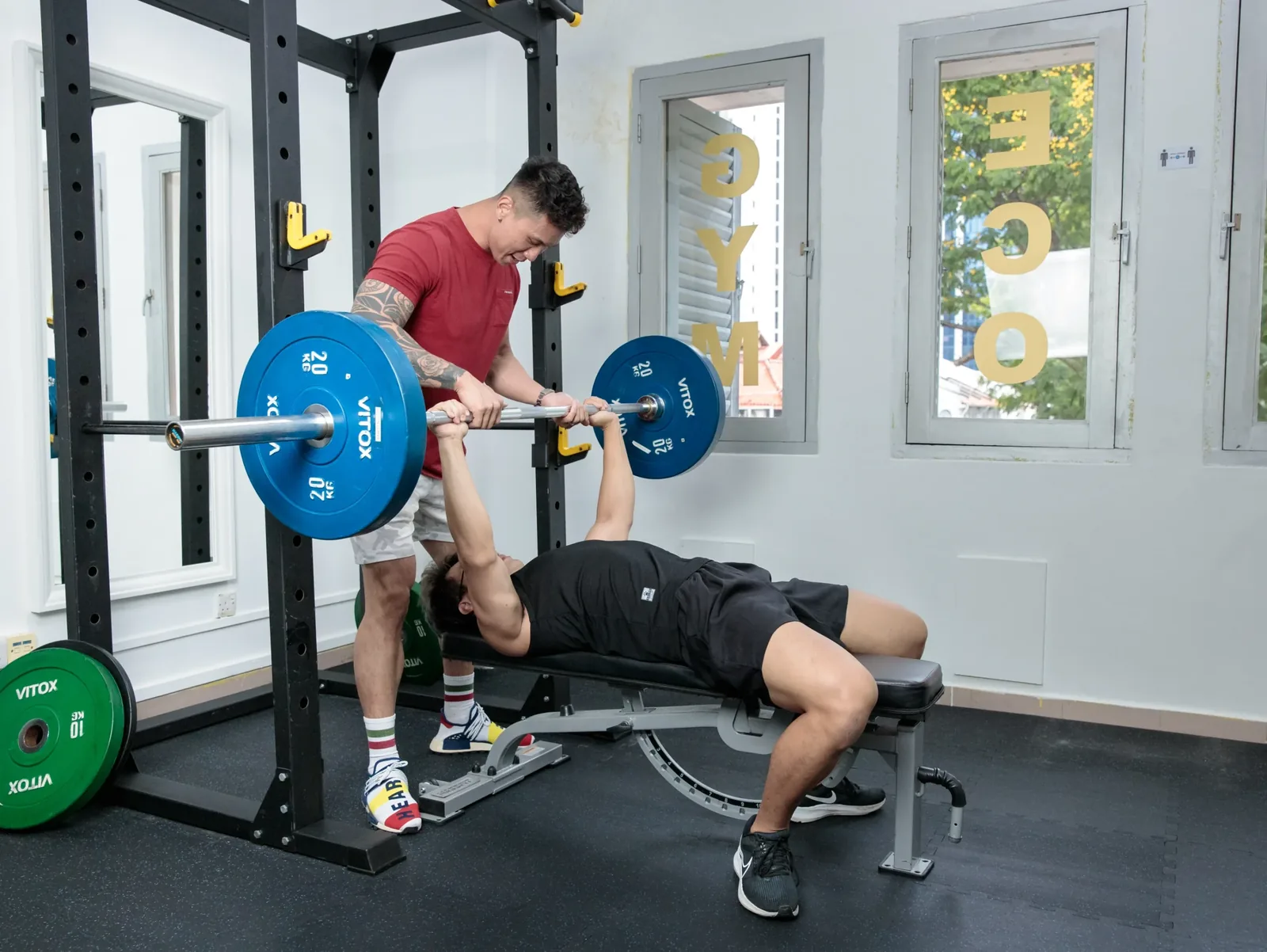 Personal trainer spotting client doing barbell bench press in gym with professional equipment