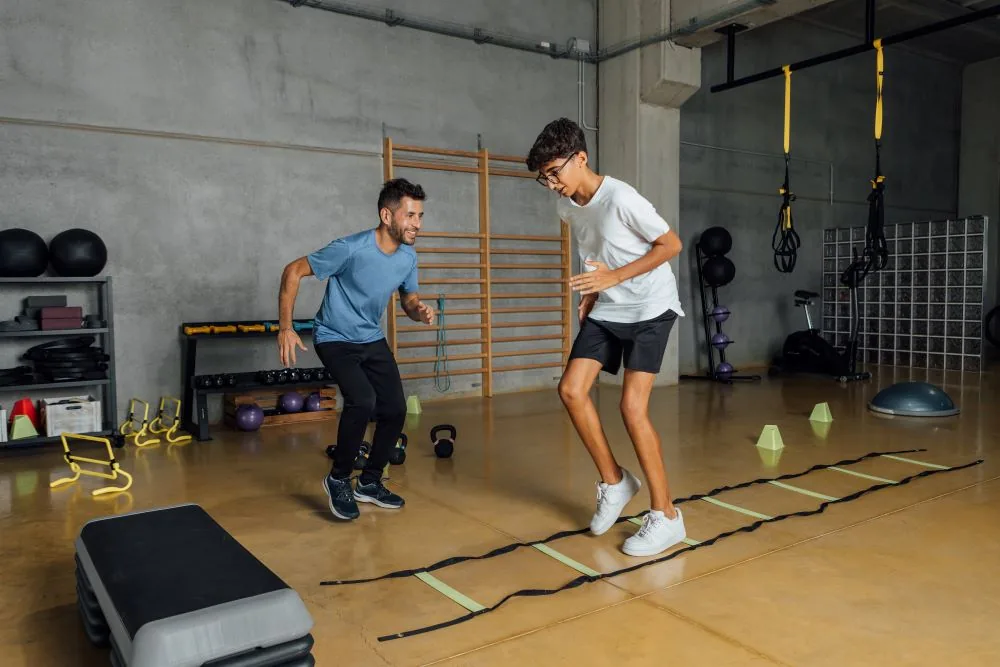 Personal trainer instructing client on agility ladder drill in fitness studio