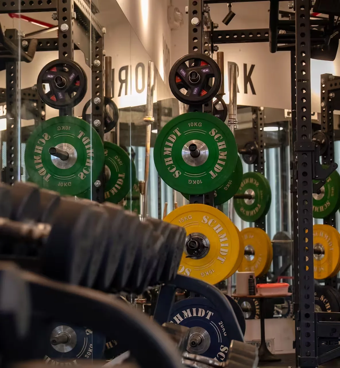 Colorful weight plates and barbells set up in a gym training area with Schmidt equipment