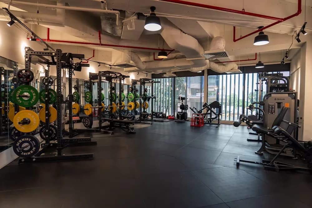 Well-lit gym interior with weight racks, plates, and cardio equipment along mirrored walls