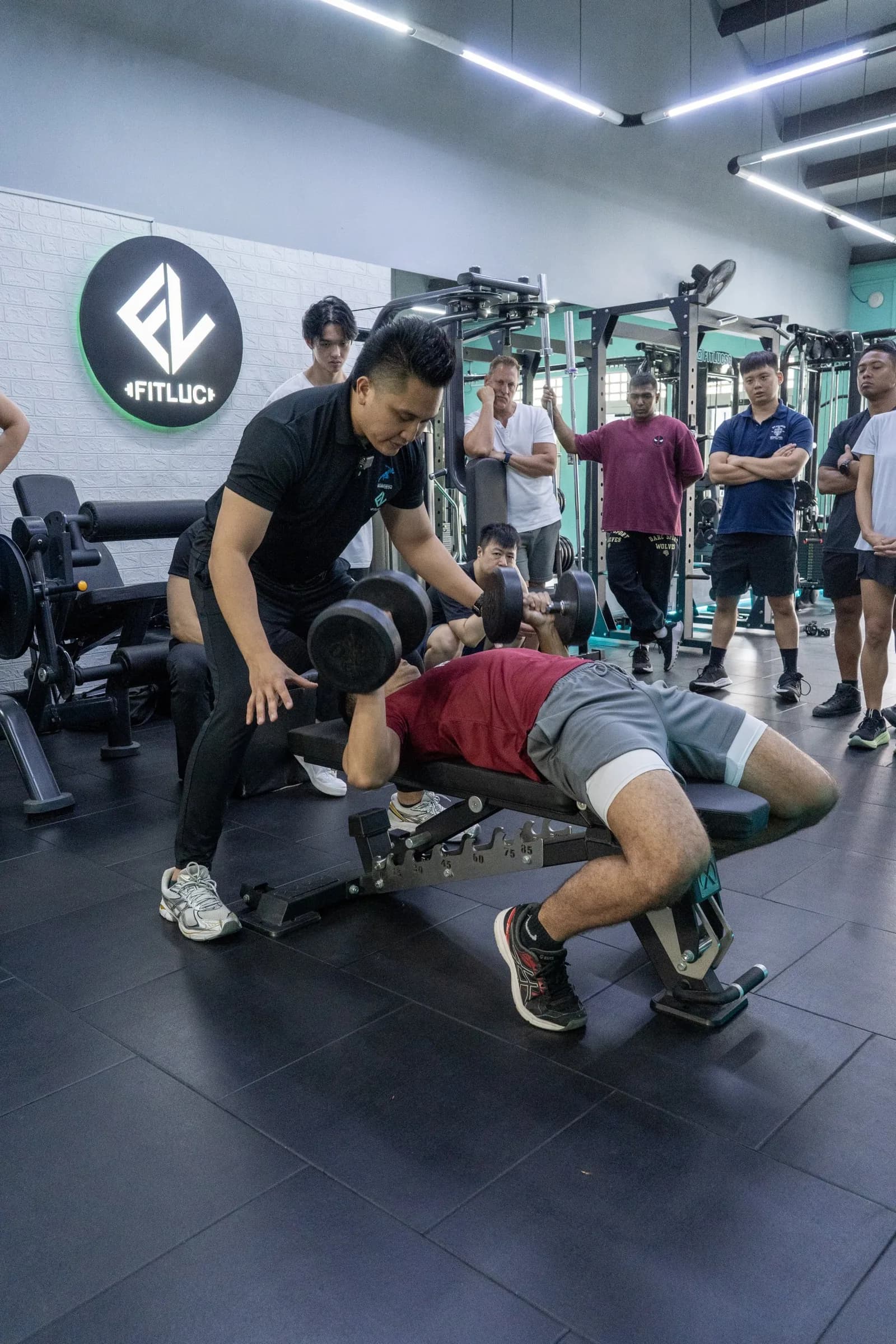 Trainer coaching client on dumbbell exercise in a modern gym with other trainees watching