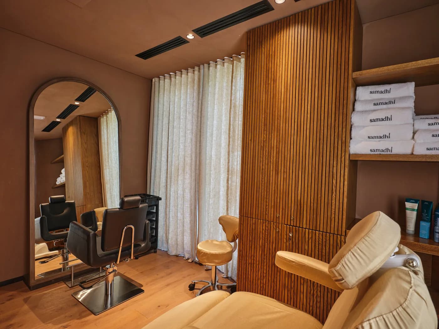Spa treatment room with wooden accents, massage chair, mirror, and Samadhi branded towels