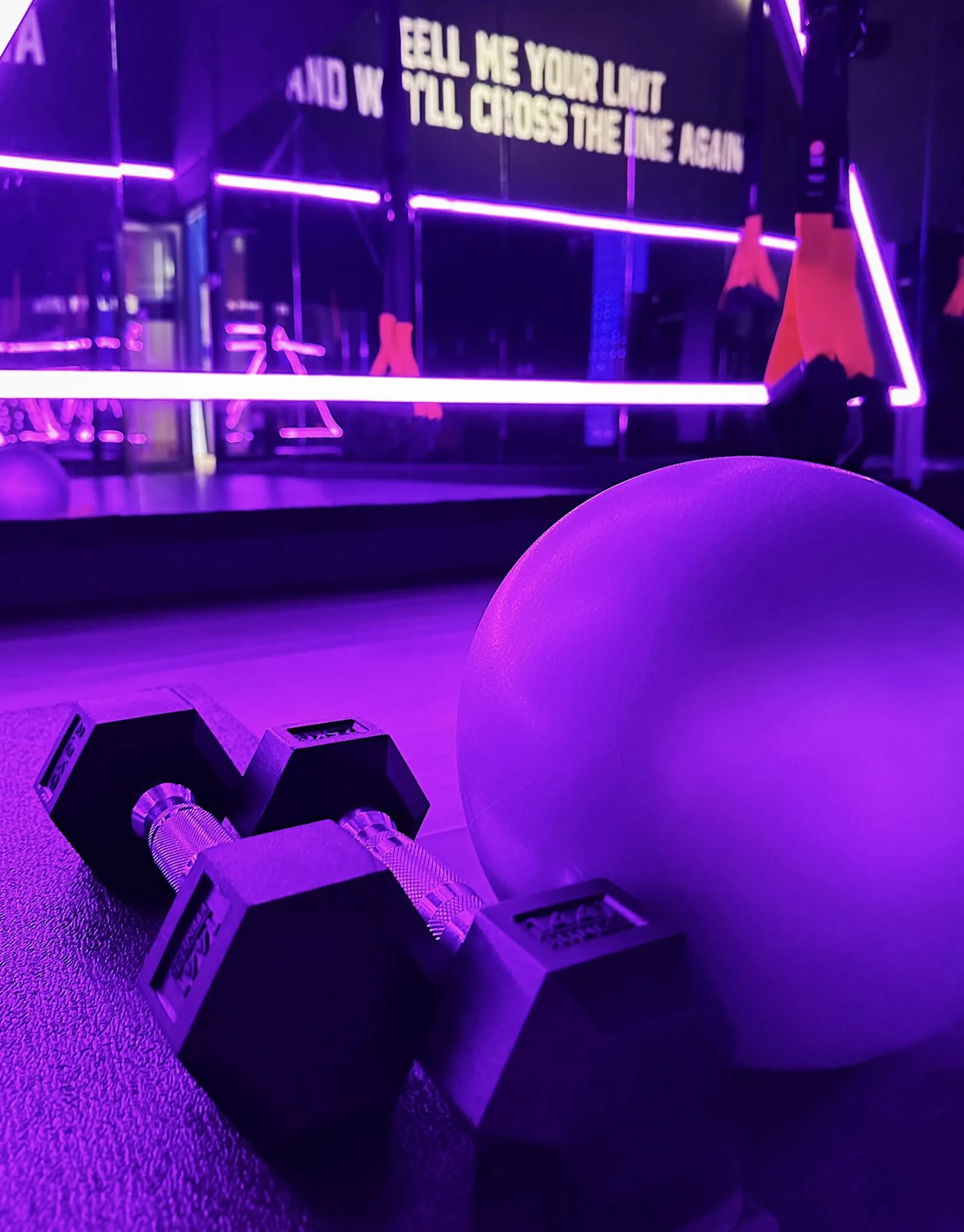 Purple-lit fitness studio interior with dumbbells, exercise ball, and neon signage