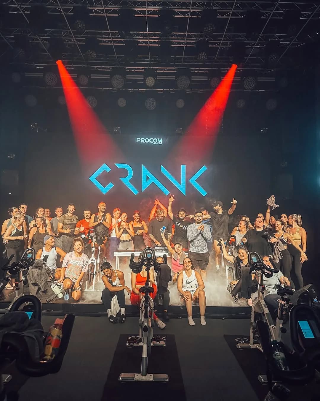 Group fitness cycling class with participants on bikes under dramatic red stage lighting
