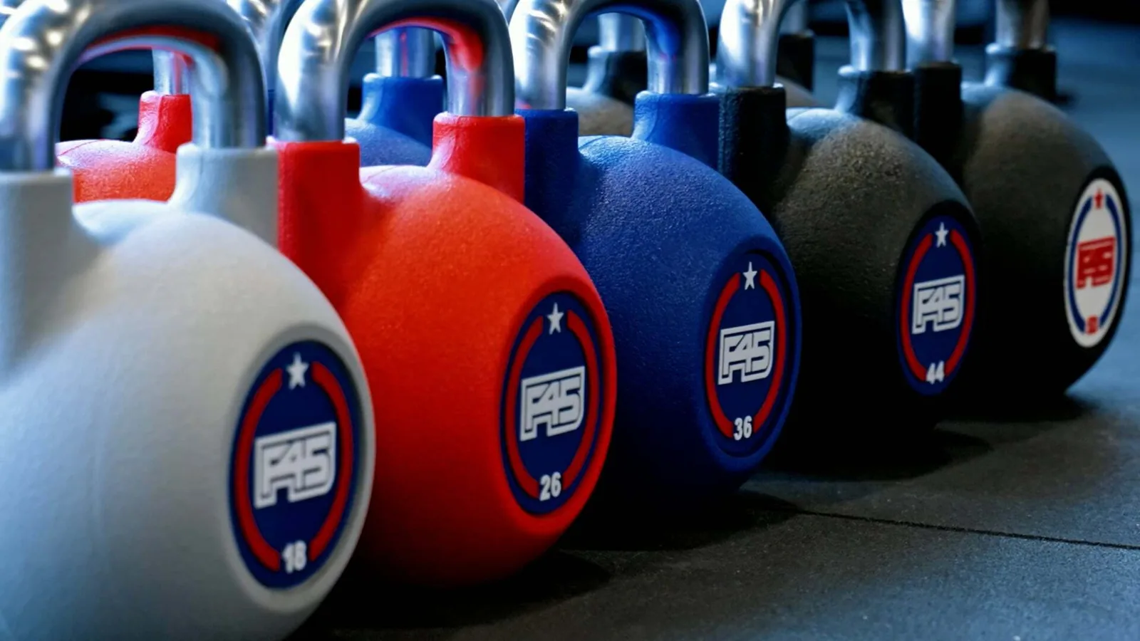 Row of F45-branded kettlebells in various colors lined up on studio floor
