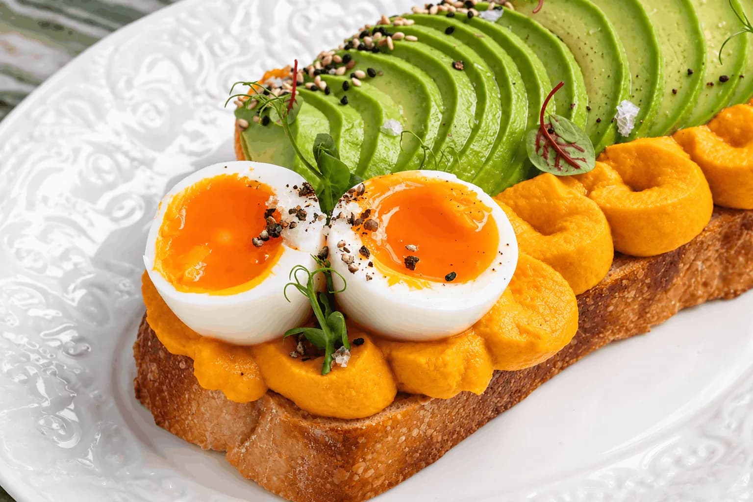 Soft-boiled egg and sweet potato toast with avocado slices and microgreens on white plate