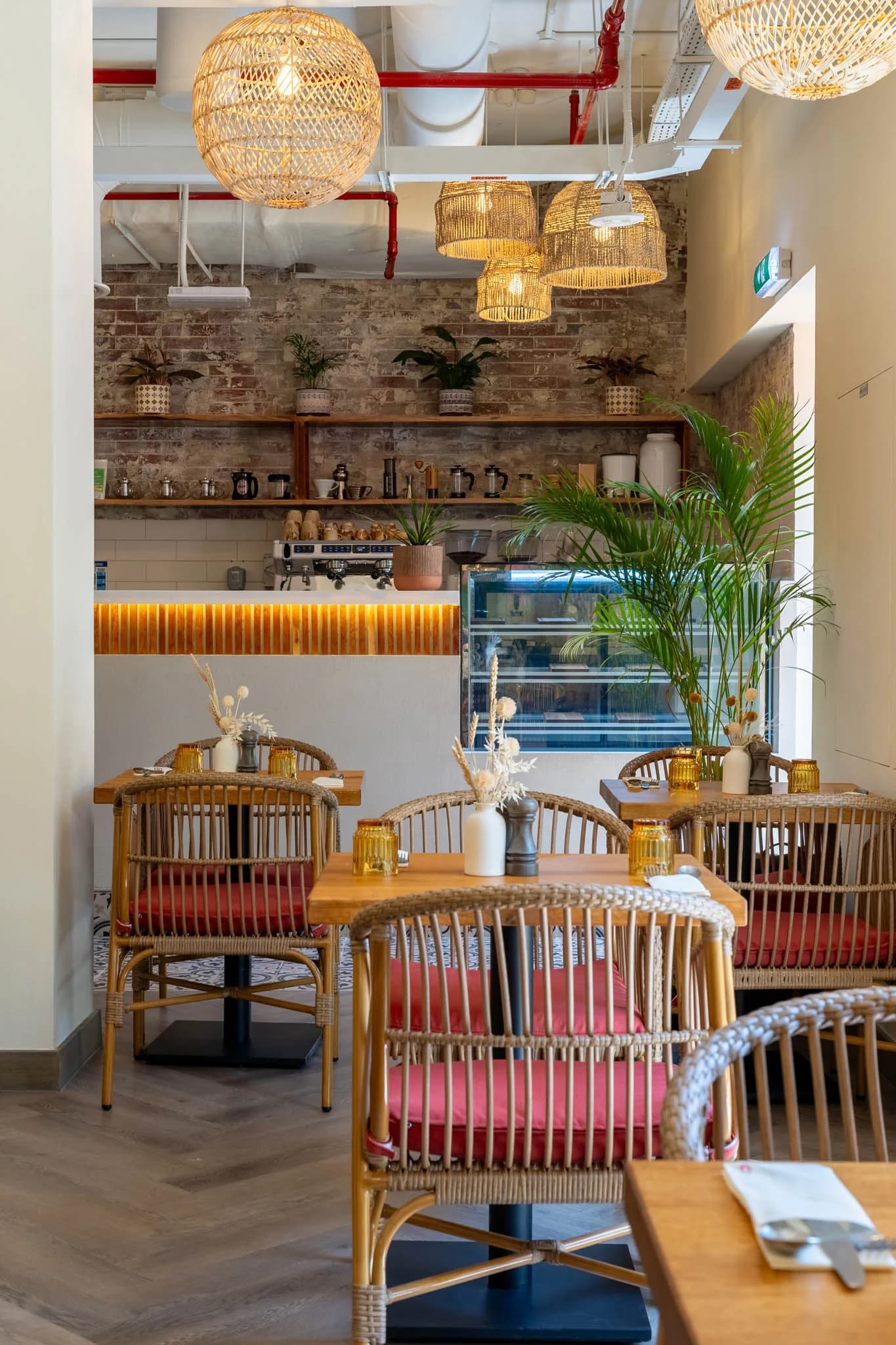 Modern café interior with rattan lighting, brick walls, wooden furniture, and plants