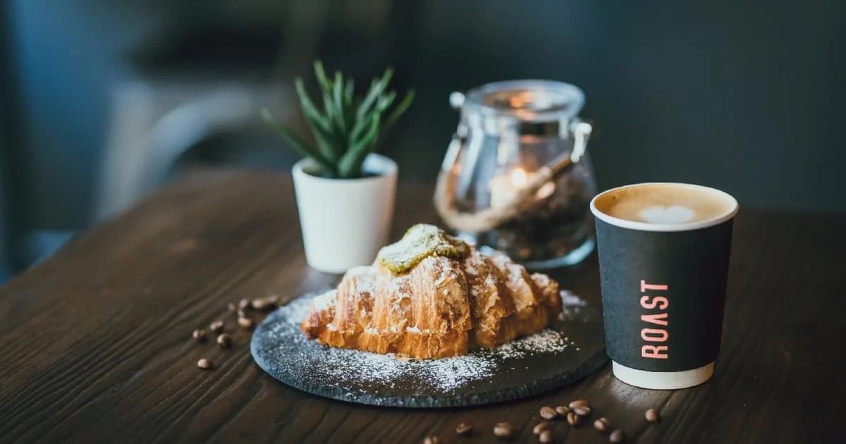 Croissant with powdered sugar, coffee cup, and plant on wooden table