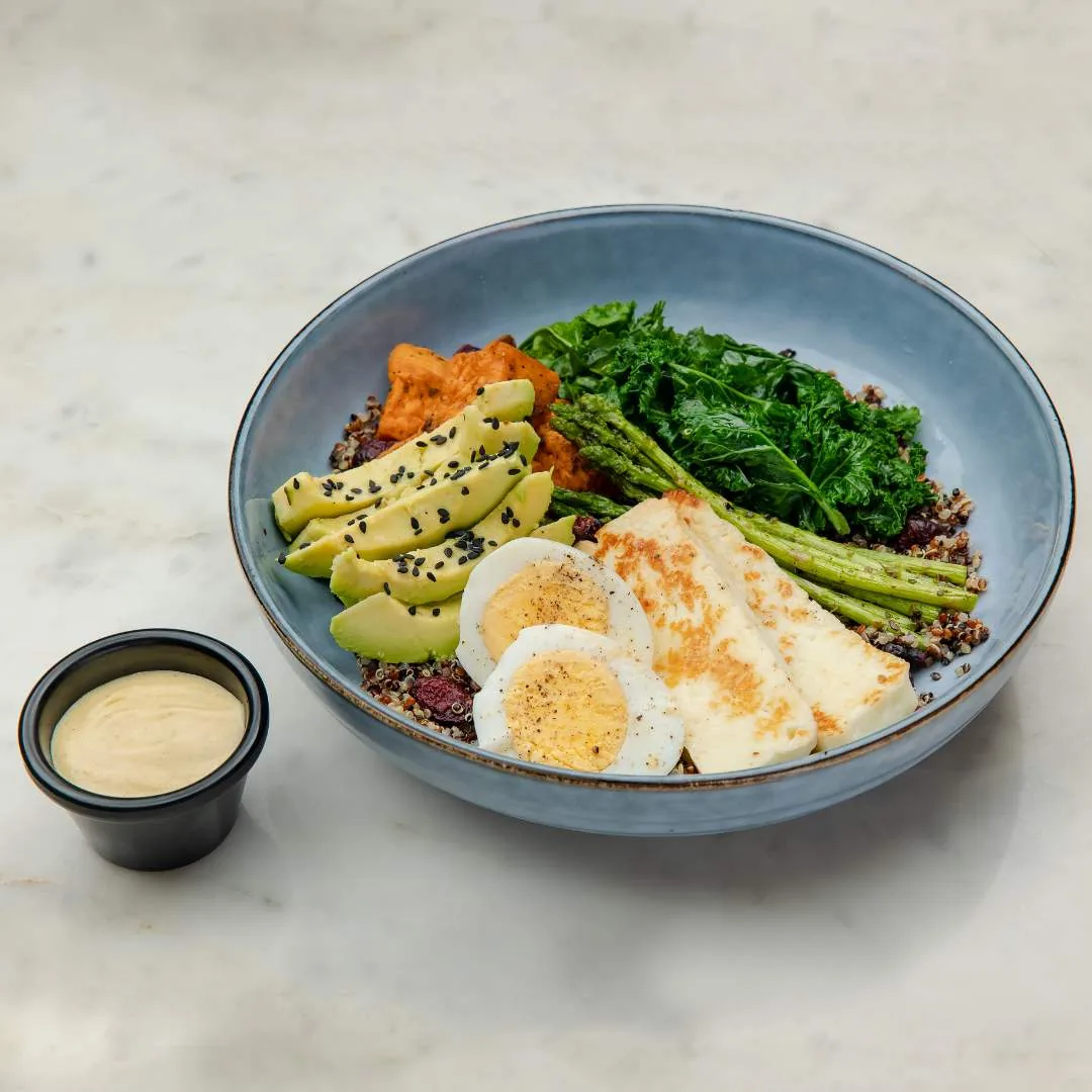 Healthy bowl with eggs, avocado, greens, sweet potato, and quinoa with dressing on the side