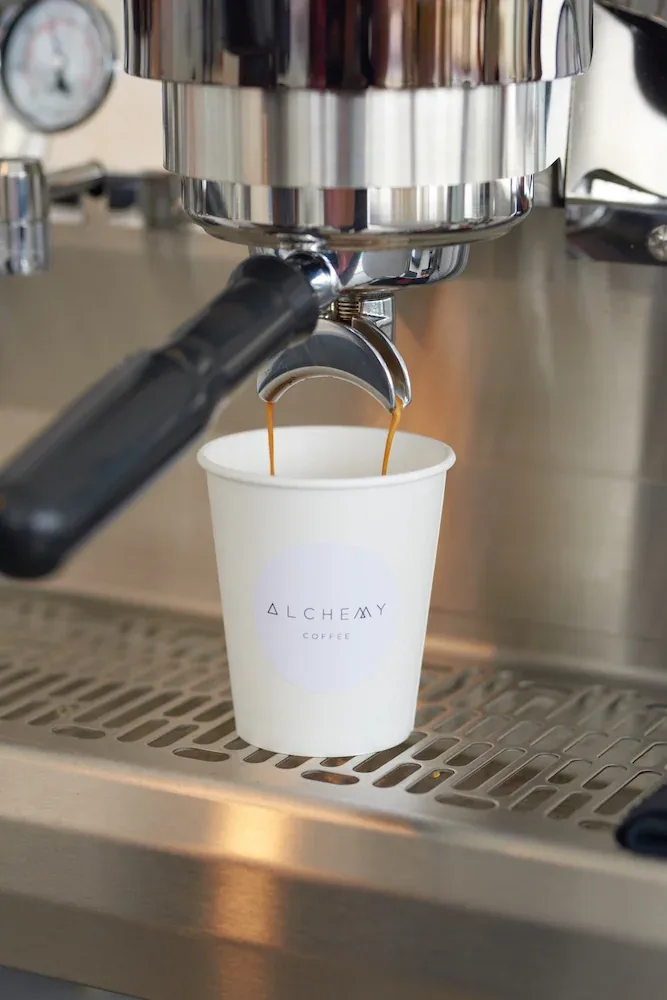 Espresso machine pouring coffee into an Alchemy Coffee branded cup