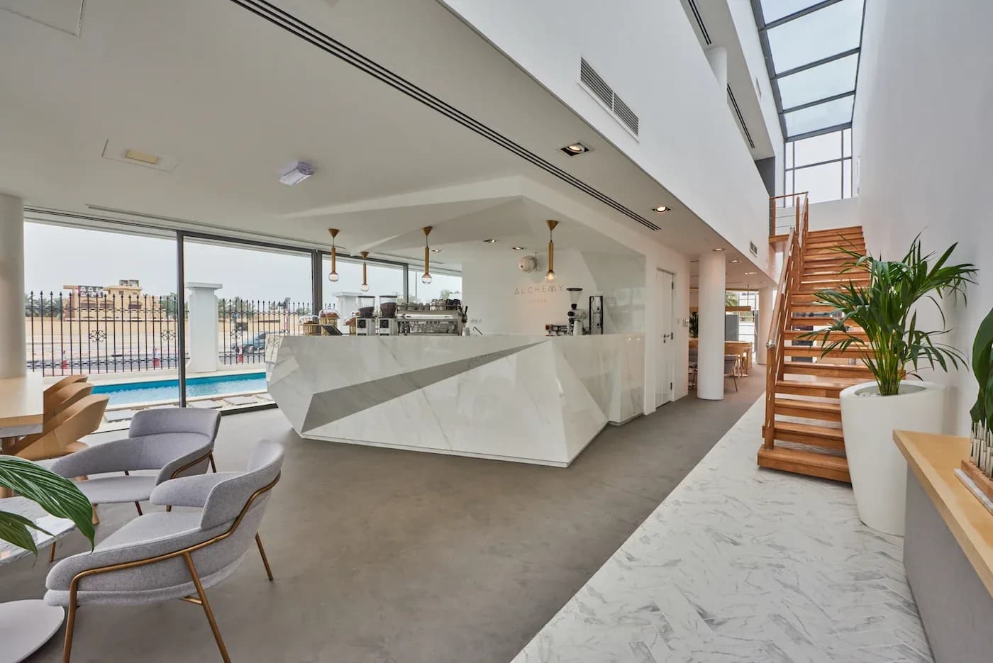 Contemporary cafe interior with white counter, grey seating, plants, and pool view through glass doors