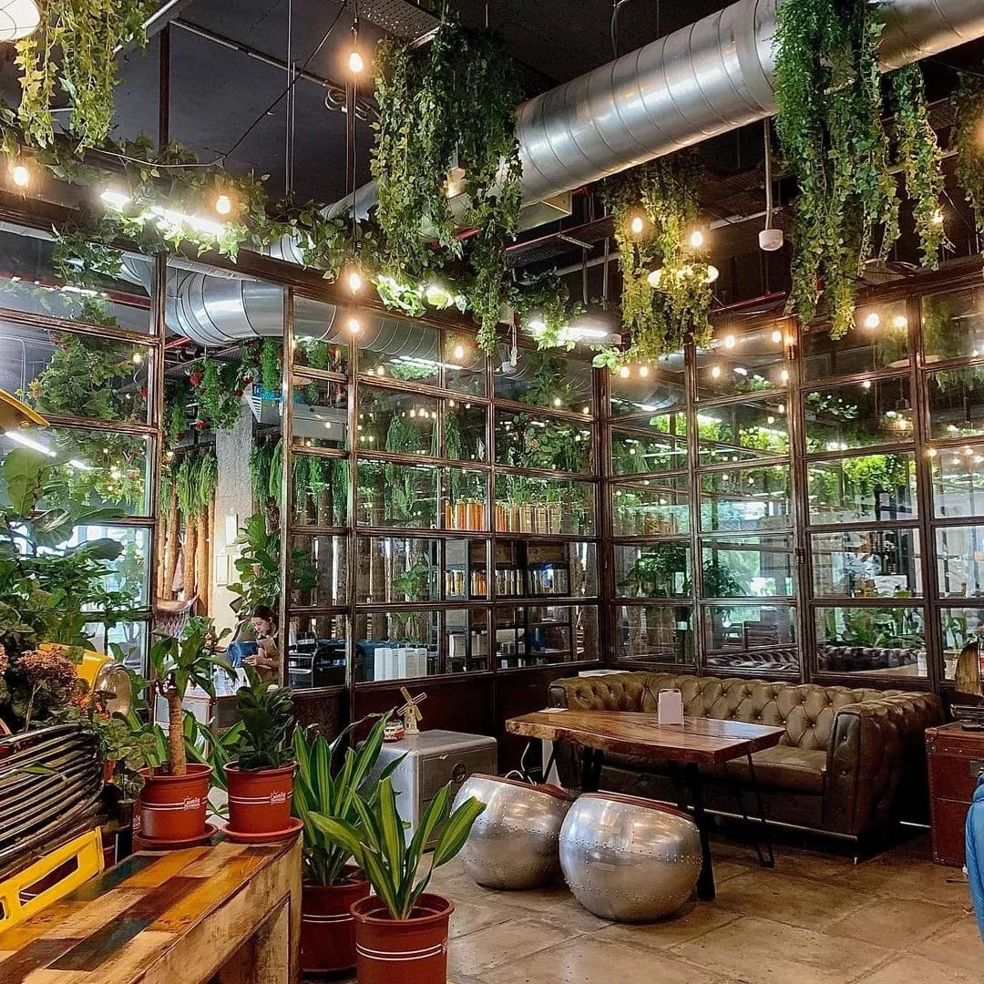 Modern salon interior with hanging greenery, brass pendant lights, leather seating, and product displays behind industrial windows