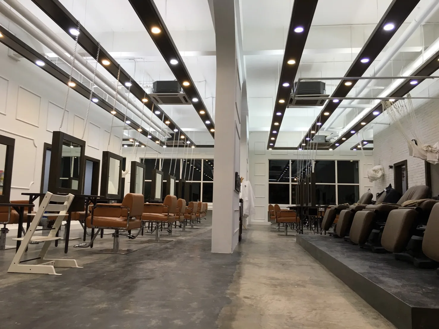 Modern hair salon interior with styling stations, mirrors, and massage chairs under contemporary lighting