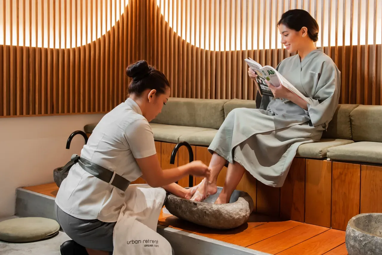 Spa therapist soaking client's feet in a stone bowl during foot treatment service.