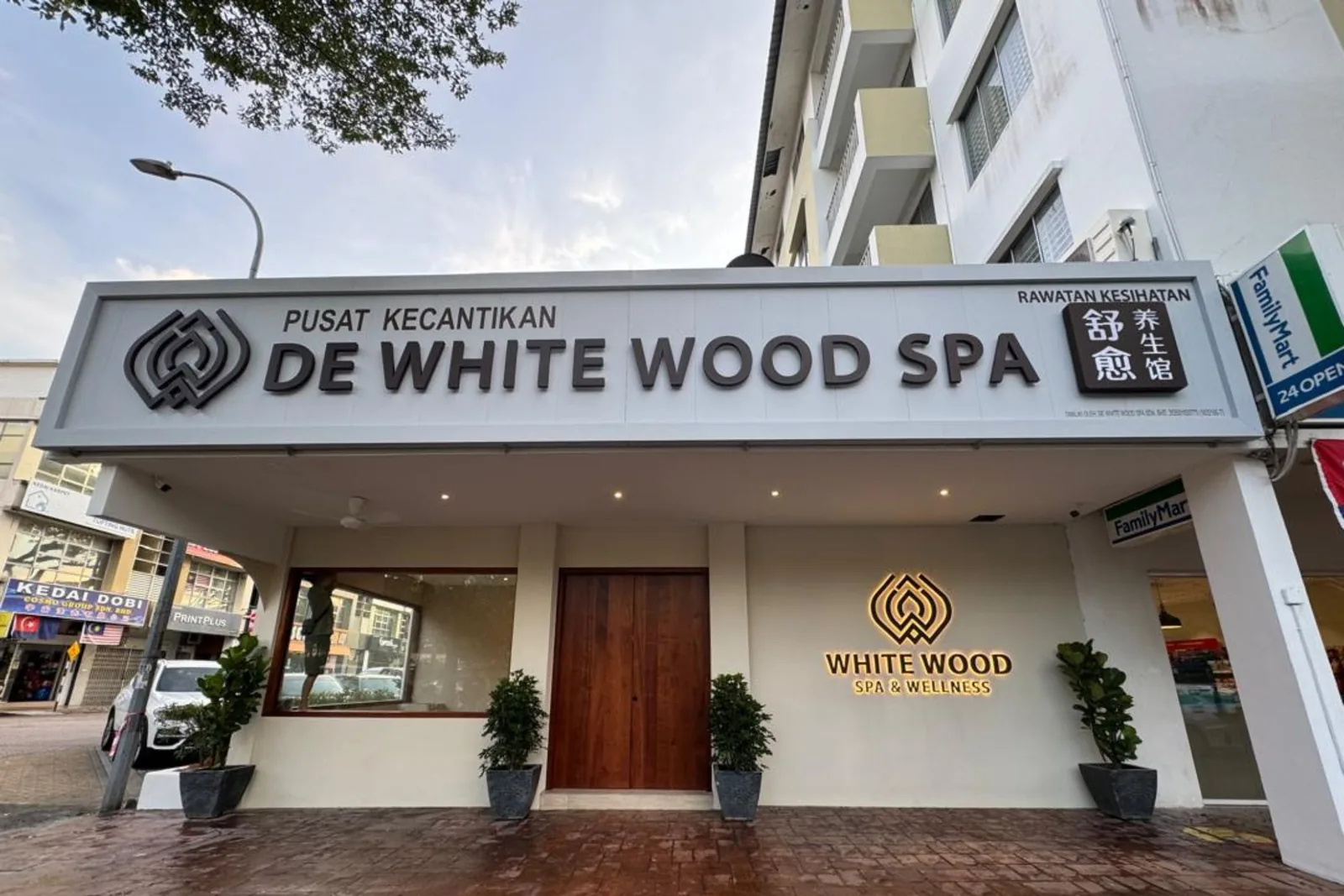 White Wood Spa storefront with logo, wooden entrance door, and potted plants on brick pavement