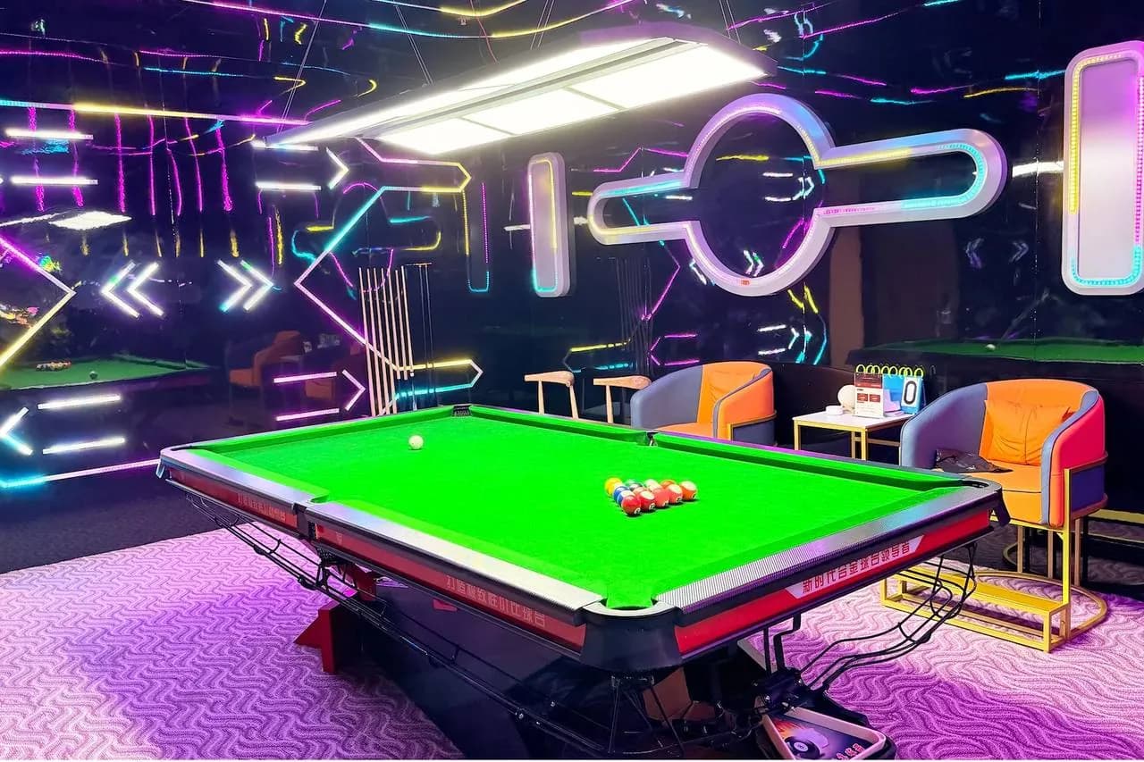 Neon-lit gaming room with green pool table and colorful wall displays
