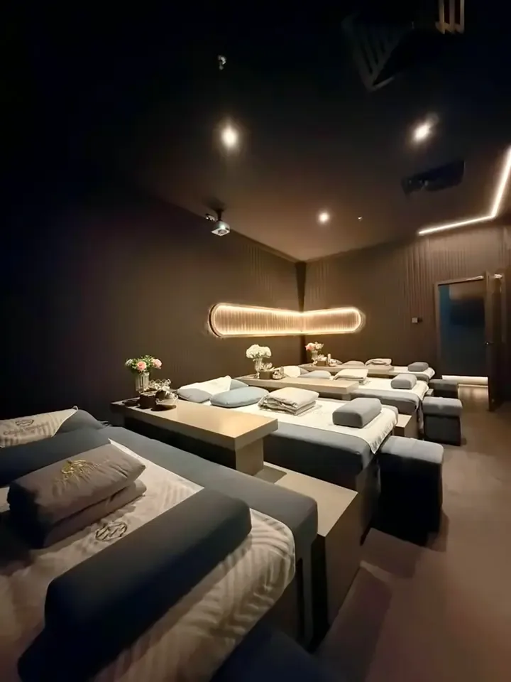 Modern spa treatment room with massage beds, neon lighting, and floral décor