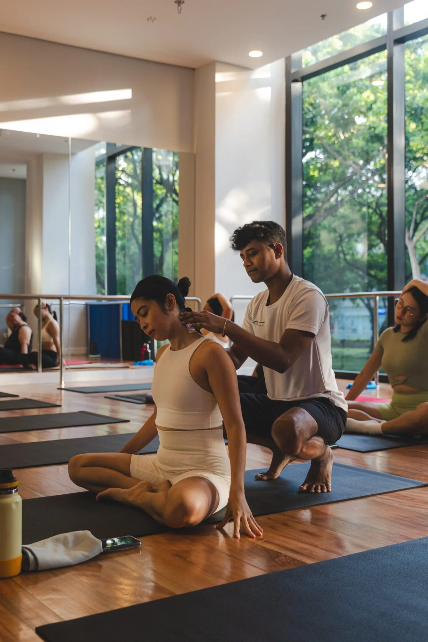 Yoga instructor adjusting student's posture during class in bright studio with windows