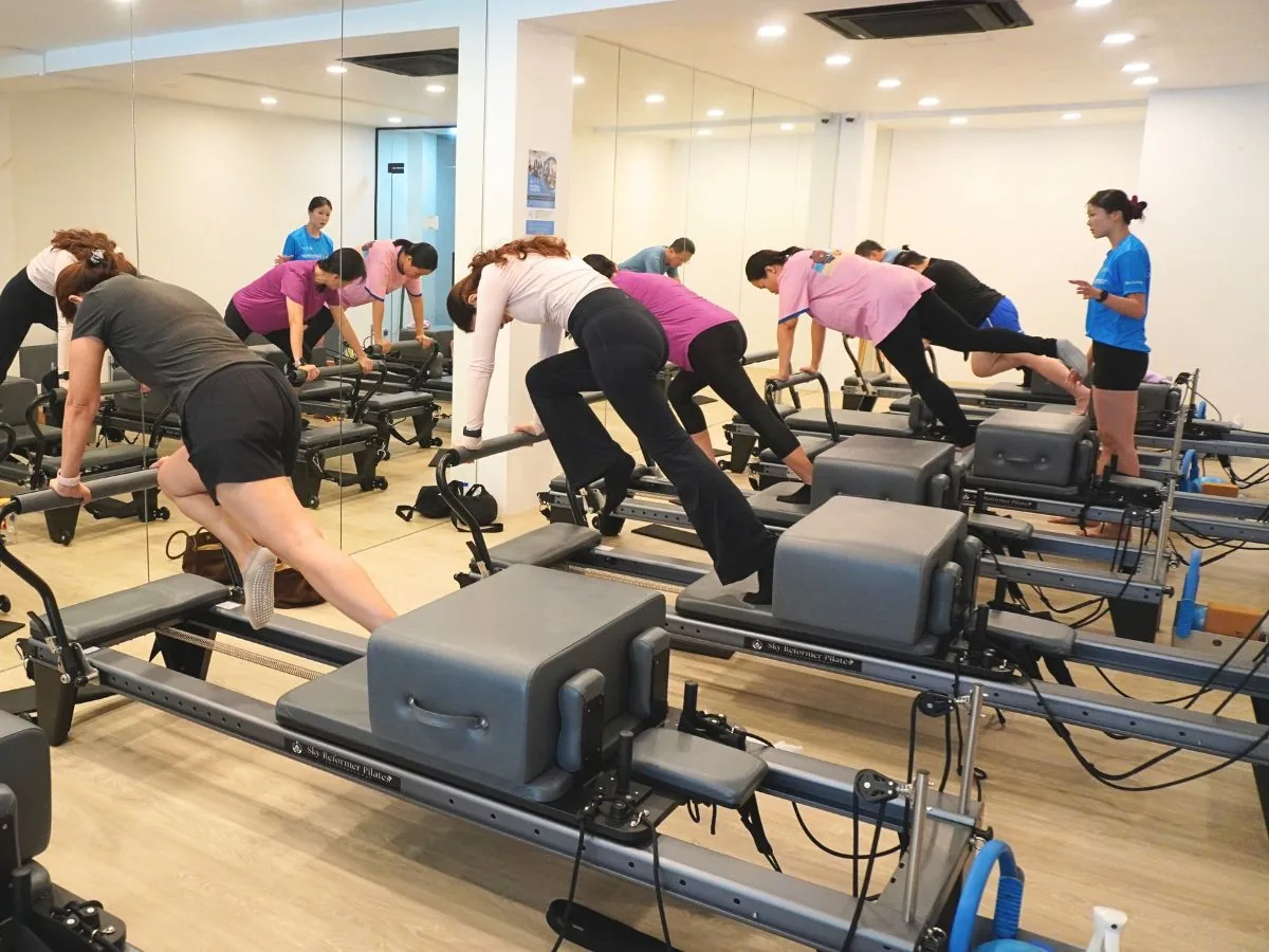 Pilates reformer class with instructor and participants exercising in a bright mirrored studio