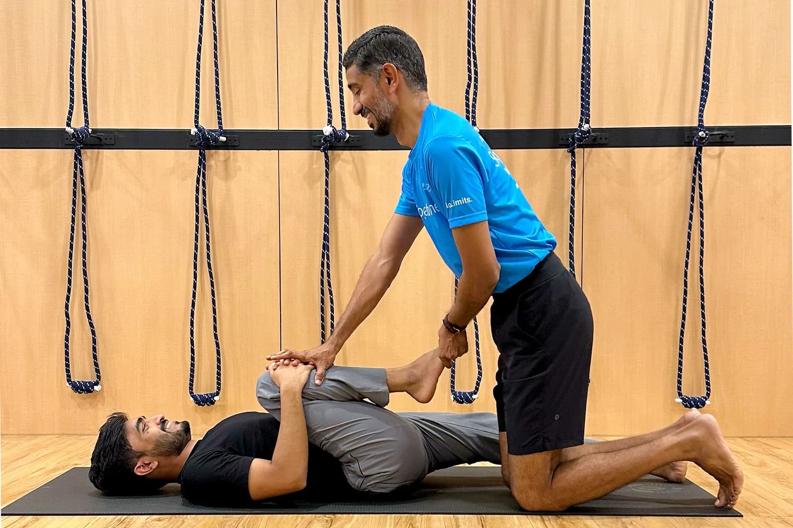 Fitness instructor assisting client with leg exercise in bright studio gym