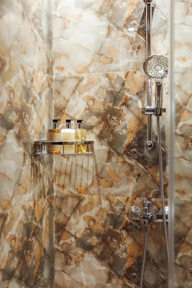 Marble shower with chrome rainfall head and amenities shelf in luxury spa bathroom