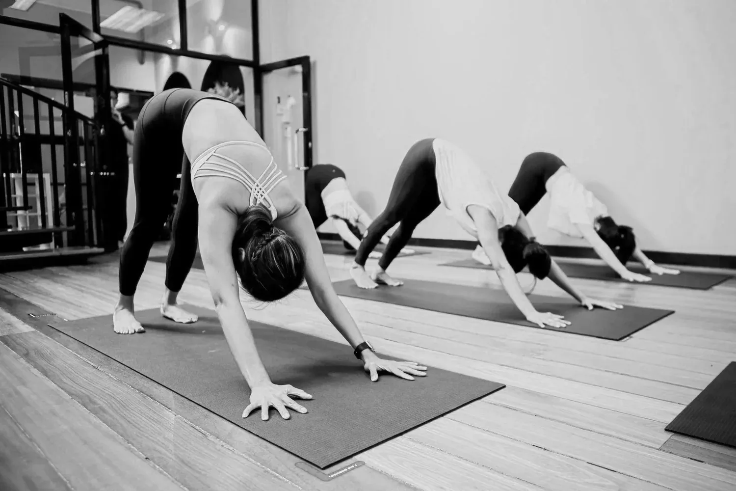 Yoga class participants in downward dog pose on mats in a bright studio space.