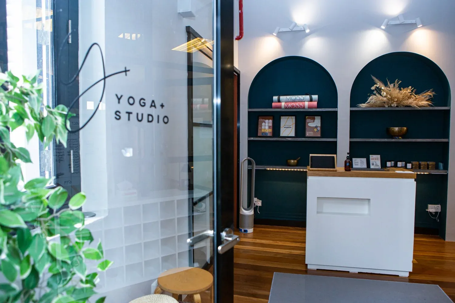 Yoga studio reception area with modern white desk, dark teal shelving, and wooden floors