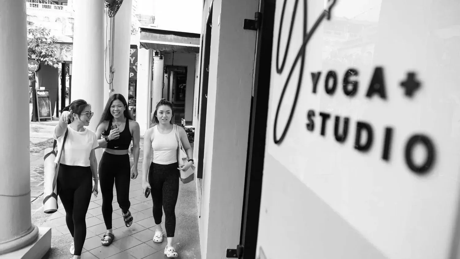 Three women in workout clothes walk out of Yoga+ Studio storefront