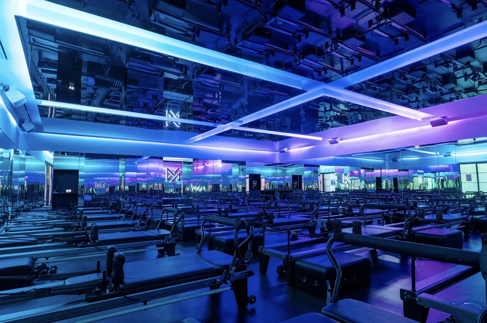 Brightly lit pilates studio with multiple reformer machines and neon blue and purple ambient lighting
